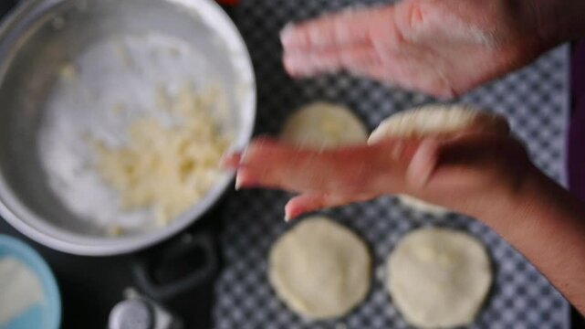 Close-up image showcasing hands forming arepa (colombian food) dough with bowls and utensils, portraying culinary preparation. Focus on background.