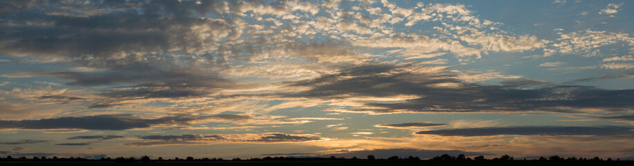 Fototapeta premium A landscape with an enchanting sunset. Panorama. Tragic gloomy sky. The last flashes of the sun on the storm clouds.