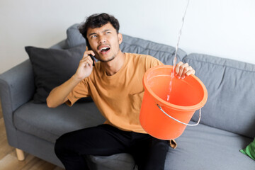 Frustrated young man looking up at water falling down from damaged ceiling in newly renovated home