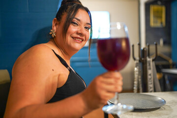 Beautiful plus size woman smiling and raising glass of red wine at restaurant