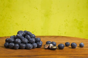 Pile of scattered blueberries on a wood table with a green background with some cut in half on a green background.