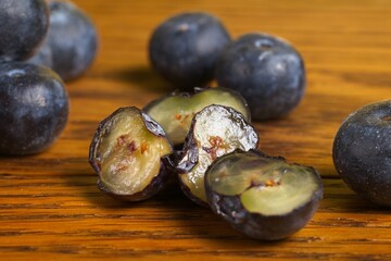 Close up of a pile of scattered blueberries on a wood table with some cut in half.