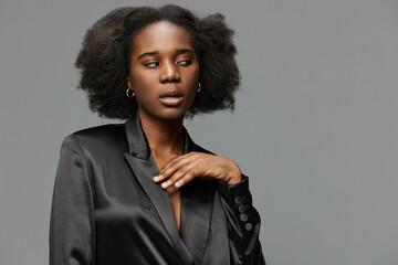 Obraz premium Stylish African model in a black satin blazer with textured hair, conveying a confident and sophisticated look against a gray background