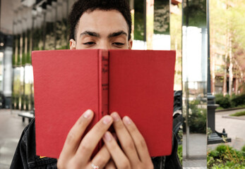 Young man reading a red book in urban park