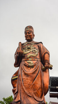 A sunning close up of Admiral Cheng Ho's statue at Sam Poo Kong Temple, Semarang. The intricate dragon details and vibrant broze color shine under the cloudy sky, symbolizing strenght and history.