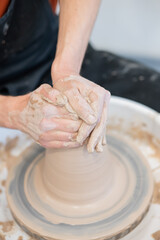 Close-up of a potter's hands working on a pottery wheel. Vertical photo. 