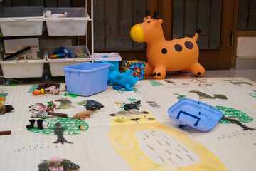 View of a child playroom with toys scattered around. There is a soft rug on the floor and boxes....