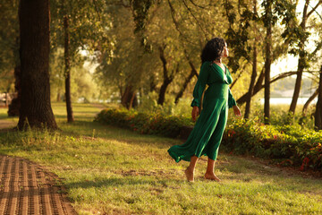 Young barefoot curly dark haired woman in green dress walking in the park