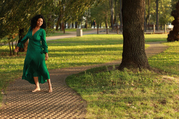 Young barefoot curly dark haired woman in green dress walking in the park