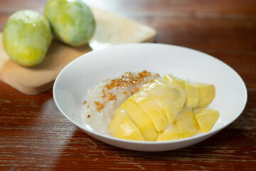 Sweet sticky rice with mango on wooden background. Mango is popular tropical fruit for dessert in Asia served with sticky rice, coconut milk. Selective focus and free copy space. Industrial food.