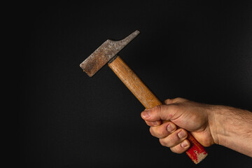 Hand holding a rusty hammer against a dark background