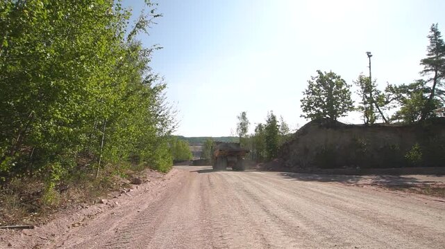 Big orange quarry truck with empty body drives on dirt road to a quarry on sunny summer day
