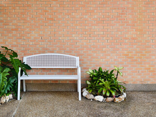A clean white metal bench is placed in front of the brick-walled.