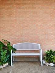 A clean white metal bench is placed in front of the brick-walled.