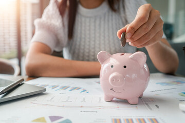 Close-up of a woman inserting a coin into a piggy bank, symbolizing savings and financial planning.