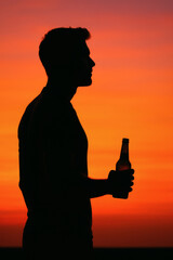 Silhouette of a man enjoying the sunset with a beverage in hand, creating a vibrant and memorable scene against the warm sky.