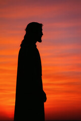 Fototapeta premium Silhouette of a person with long hair and a crown, set against a sunset backdrop creating a religious and contemplative scene.