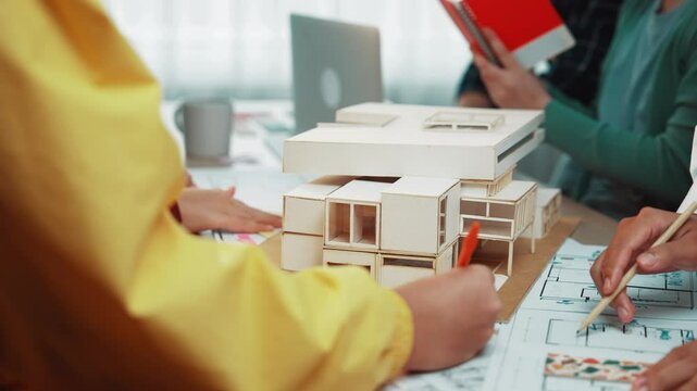 Dynamic team meeting in a modern office, focusing on architectural design and strategy, featuring a model, blueprints, and tools scattered on the table for collaboration. SACTR