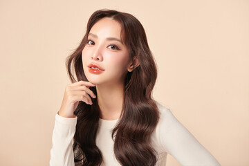 Fototapeta premium A beautiful young Asian woman with clean, fresh skin against a beige background. Skincare, facial treatment, cosmetology, beauty, and spa. An elegant portrait of an Asian woman.