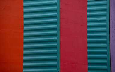 close up of sides of shipping containers painted red green  turquoise purple standing on end showing smooth red side and green corrugated metal side colorful horizontal backdrop background wallpaper 