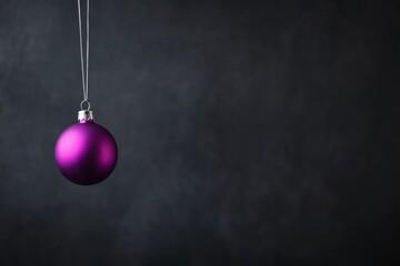 A single glossy purple ornament sphere dangles from a silver thread, reflecting light against a softly blurred neutral background. Space for text is available