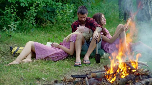 Outdoor camping with friends. Young people rest on camping near bonfire. Tourists rest at campsite on camp. Rest on summer camping trip. Relaxing by the fire after a long hike. Campfire fun.