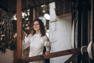 Beautiful young brunette woman in a white dress on the veranda of the house
