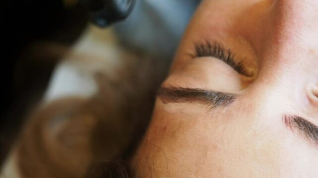 extreme close-up in slow motion shows gloved hands adjusting the skin near the eyebrow, captureing control, gentleness, and the detailed rhythm of an advanced microblading technique