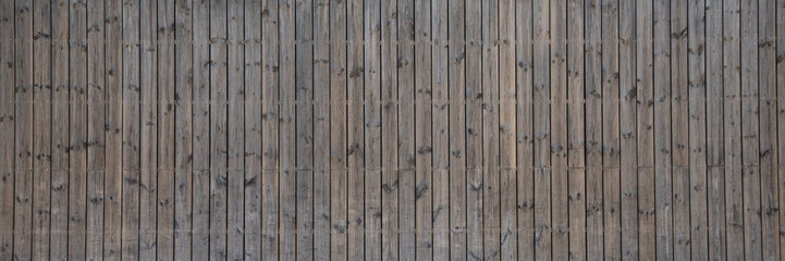Fototapeta na wymiar wooden long vertical wall facade fence made of planks line wood brown background in web panoramic header large panorama