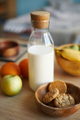 Close-up of glass bottle filled with milk, wooden bowl with cookies, and assortment of fruits on wooden table inside kitchen enjoying cozy atmosphere