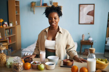 Portrait of African American woman smiling while preparing breakfast in cozy kitchen. Sustainable...