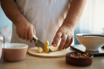 Close-up of person slicing vegetables on wooden cutting board in cozy kitchen setting with various kitchen utensils on counter