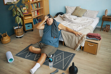 Middle-aged man engaging in workout routine on a floor mat in cozy bedroom setting, surrounded by...