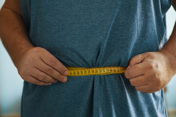 Hands holding yellow measuring tape around waist while wearing blue shirt