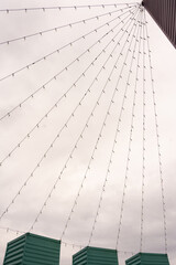 many strings of light bulbs strung from the tops of three green containers on end to a higher top of a black building creating triangular shapes conceptually interesting vertical image 