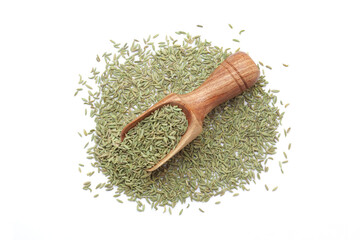 A wooden scoop filled with organic Small Fennel Seeds (Foeniculum vulgare), placed on a heap of fennel seeds, isolated on a white background.
