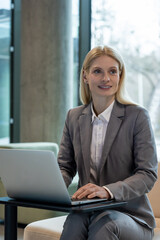 Stylish businesswoman sitting in sofa working with laptop in modern hall