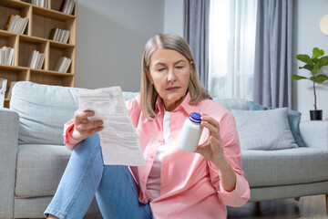 Mid aged woman in pink shirt reading description to medicine and looking concentrated