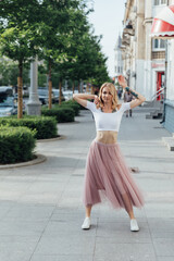 blonde woman in dress dancing to music alone on city street