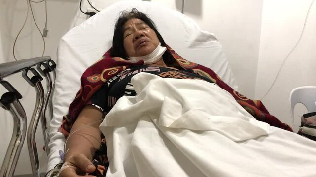 mature woman lies in a hospital bed with a dextrose IV attached to her right hand.