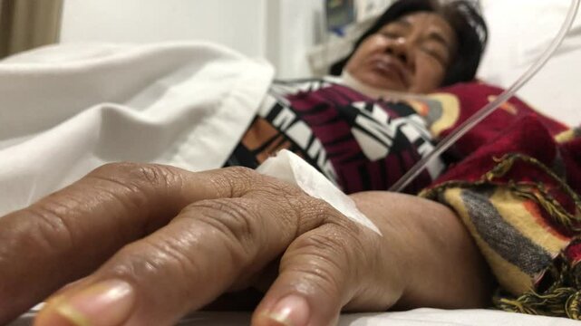 mature woman lies in a hospital bed with a dextrose IV attached to her right hand.