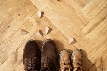 Concept Father day greeting card. Man and children shoes, craft paper hearts on the wooden oak parquet flooring background top view.