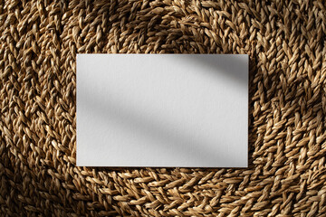 Clean blank card with sunlight shadows on natural jute background. Neutral composition for minimalistic brand template in flat lay style.