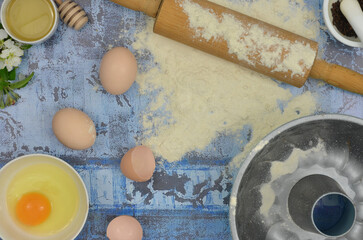 Flour and eggs on the table, top view blue kitchen table: flour, eggs, yolk, rolling pin, cake tin and delicacies.