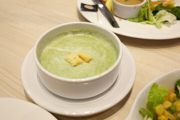 Green spinach soup in a white bowl with a saucer on the dining table.