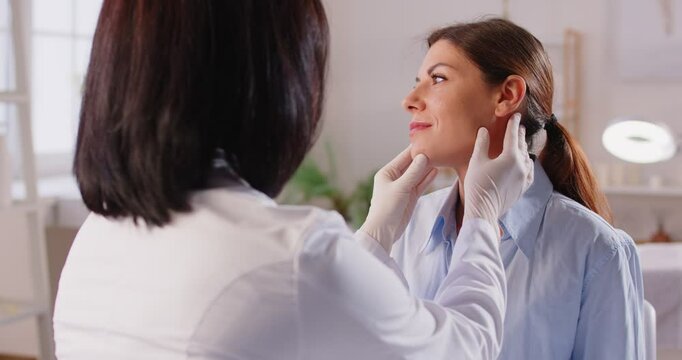 Female surgeon touching woman face consulting before rhinoplasty operation. Beautician or cosmetologist examining skin condition to a young girl client. Plastic surgery and beauty concept. 4k video.