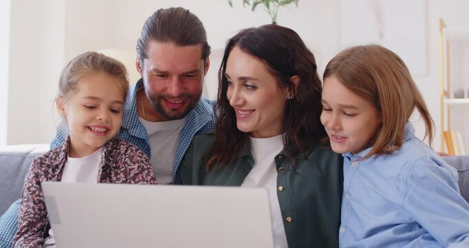 Happy family online, parents with daughter and son using laptop sitting at home, smiling mother, father and cute children looking at laptop screen planning using video call, having fun with computer