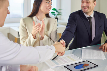 Group of a young smart three business people sitting in modern office and making a deal shaking hands with colleagues on meeting. Coworkers and employees reaching agreement. partnership concept.