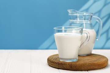 Fresh milk into glass cup and pitcher placed on wooden board against vibrant blue backdrop
