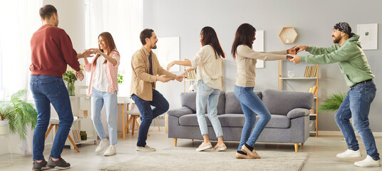 Group of happy friends dancing together at home during a weekend party, celebrating with lively music and entertainment. Fun atmosphere, sharing joyful moments in a relaxed and cheerful setting.